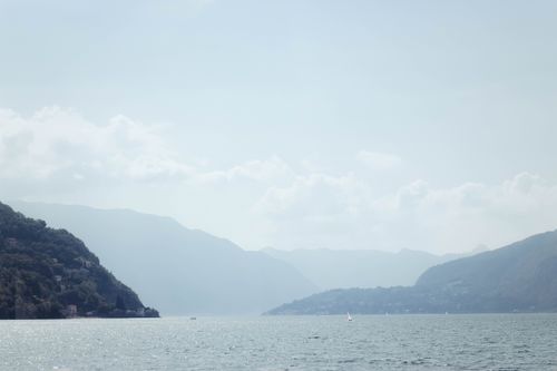Free Serene panorama of misty Lake Como in Lombardy, Italy with mountains and calm waters. Stock Photo
