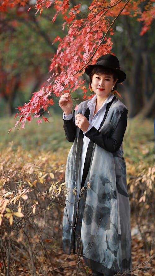 A Woman in Black and White Dress with Black Hat Under Maple Tree