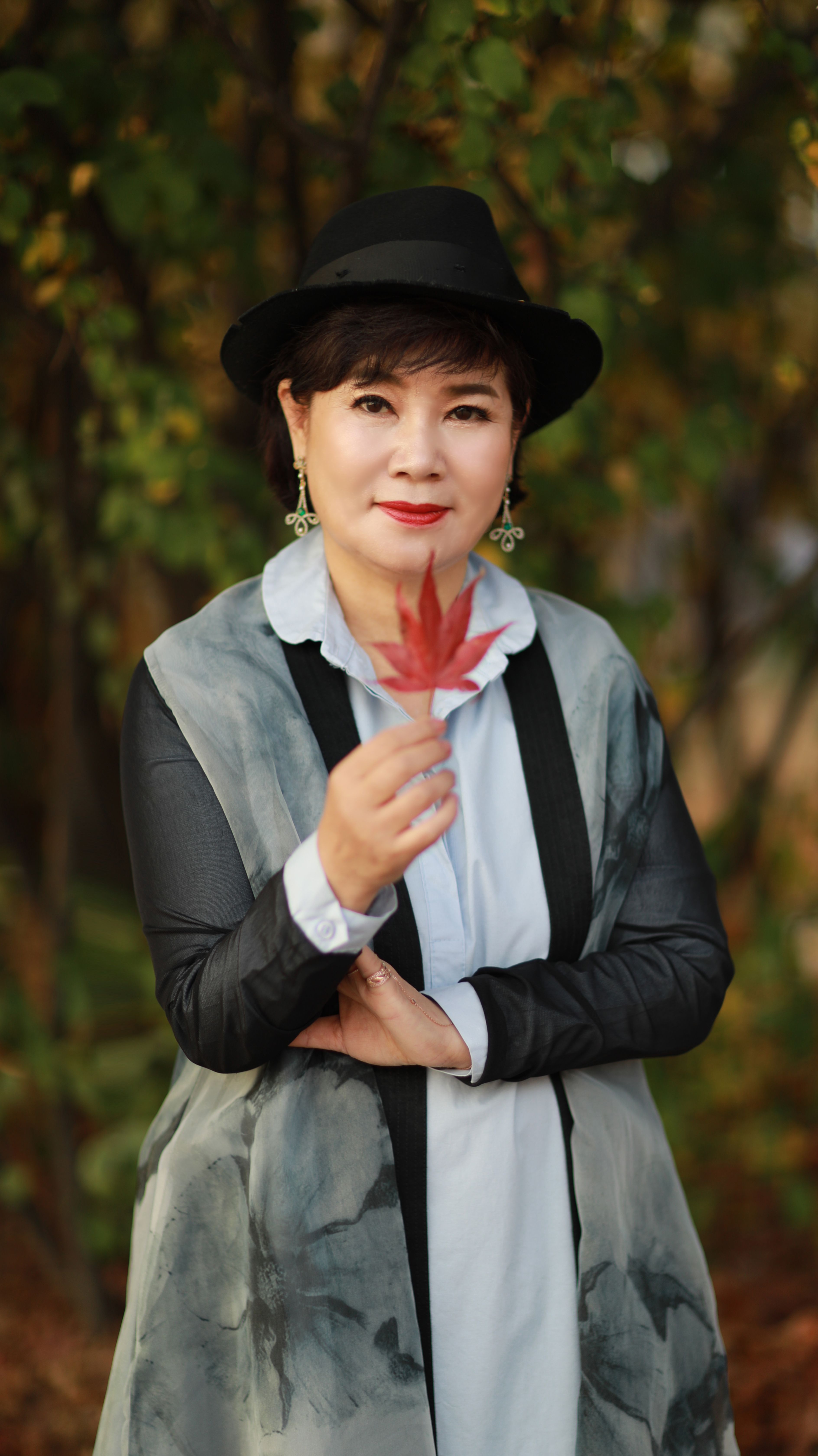 Portrait of a fashionable woman outdoors holding a red leaf, showcasing autumn fashion.