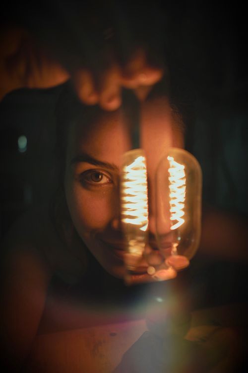 Free Woman holding an illuminated light bulb, casting a warm glow Stock Photo