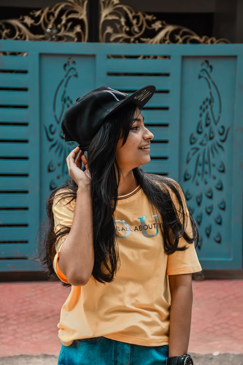 Free Young woman wearing a yellow shirt and cap, smiling outdoors against a decorative gate. Stock Photo