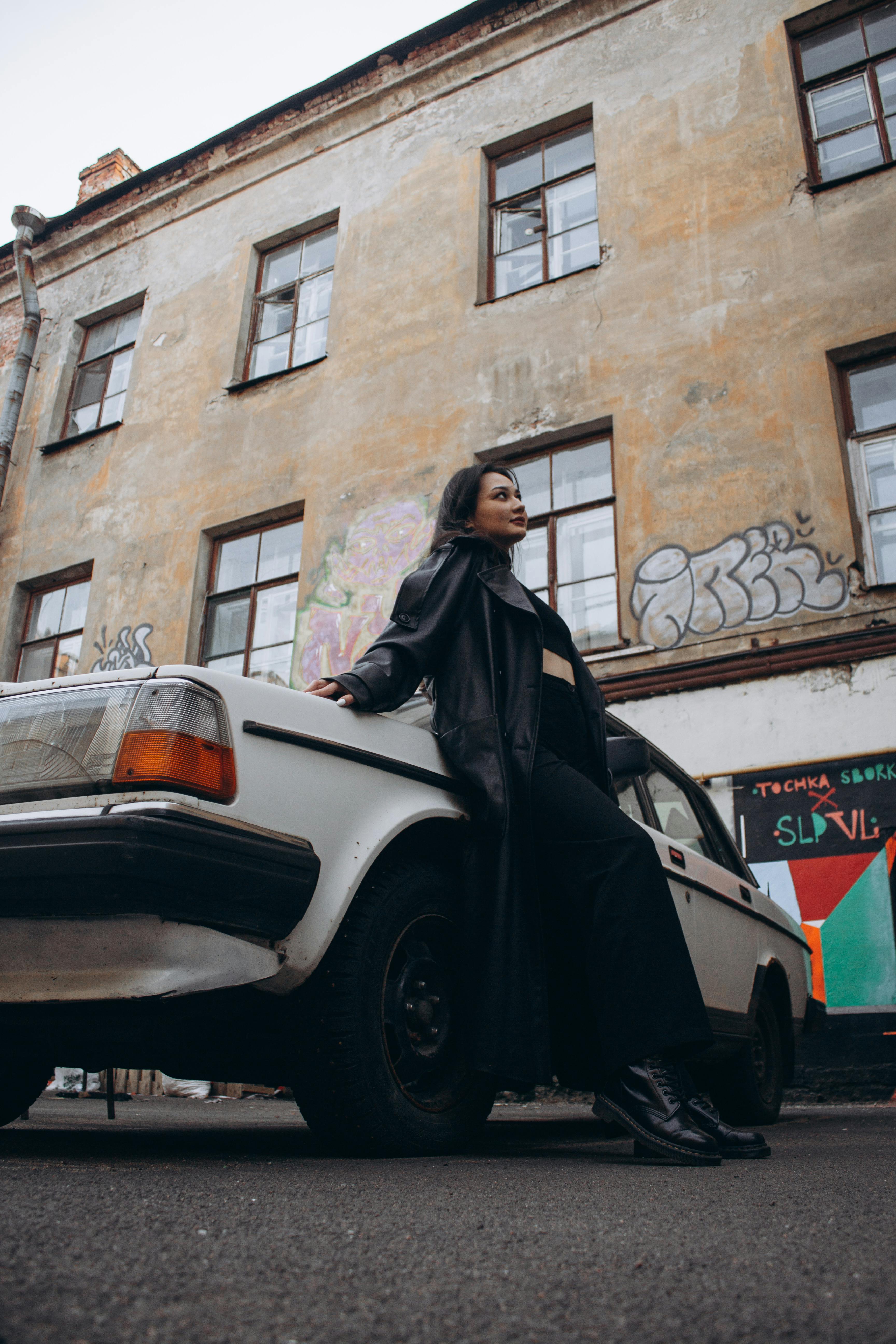 woman in black long coat standing beside white car