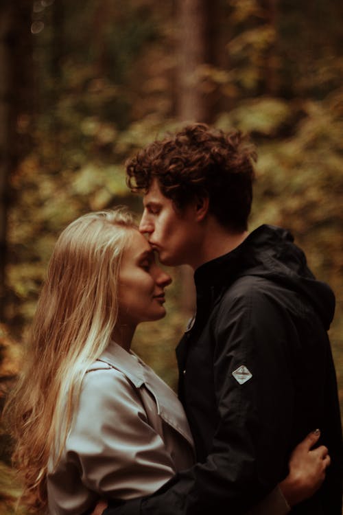 Free A couple shares an intimate moment, kissing amidst a serene forest backdrop. Stock Photo