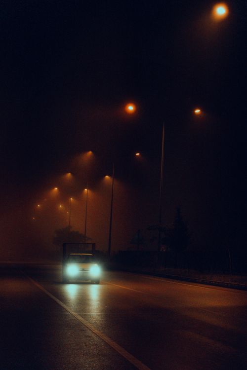 Free A car drives on a dimly lit street at night under glowing streetlamps. Stock Photo