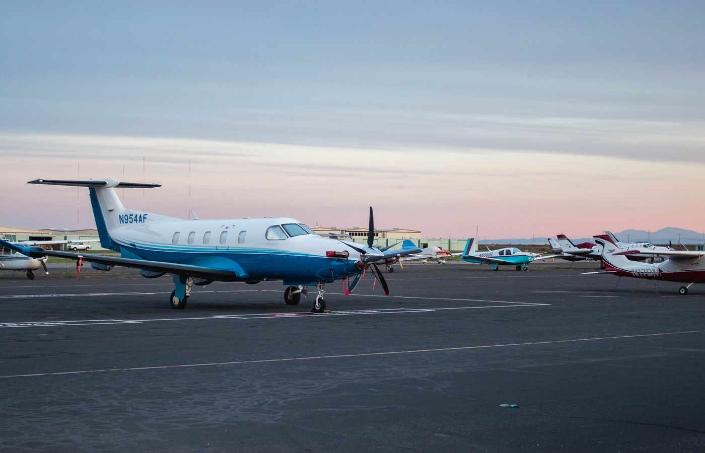 A serene view of private jets lined up on an airport runway during twilight.