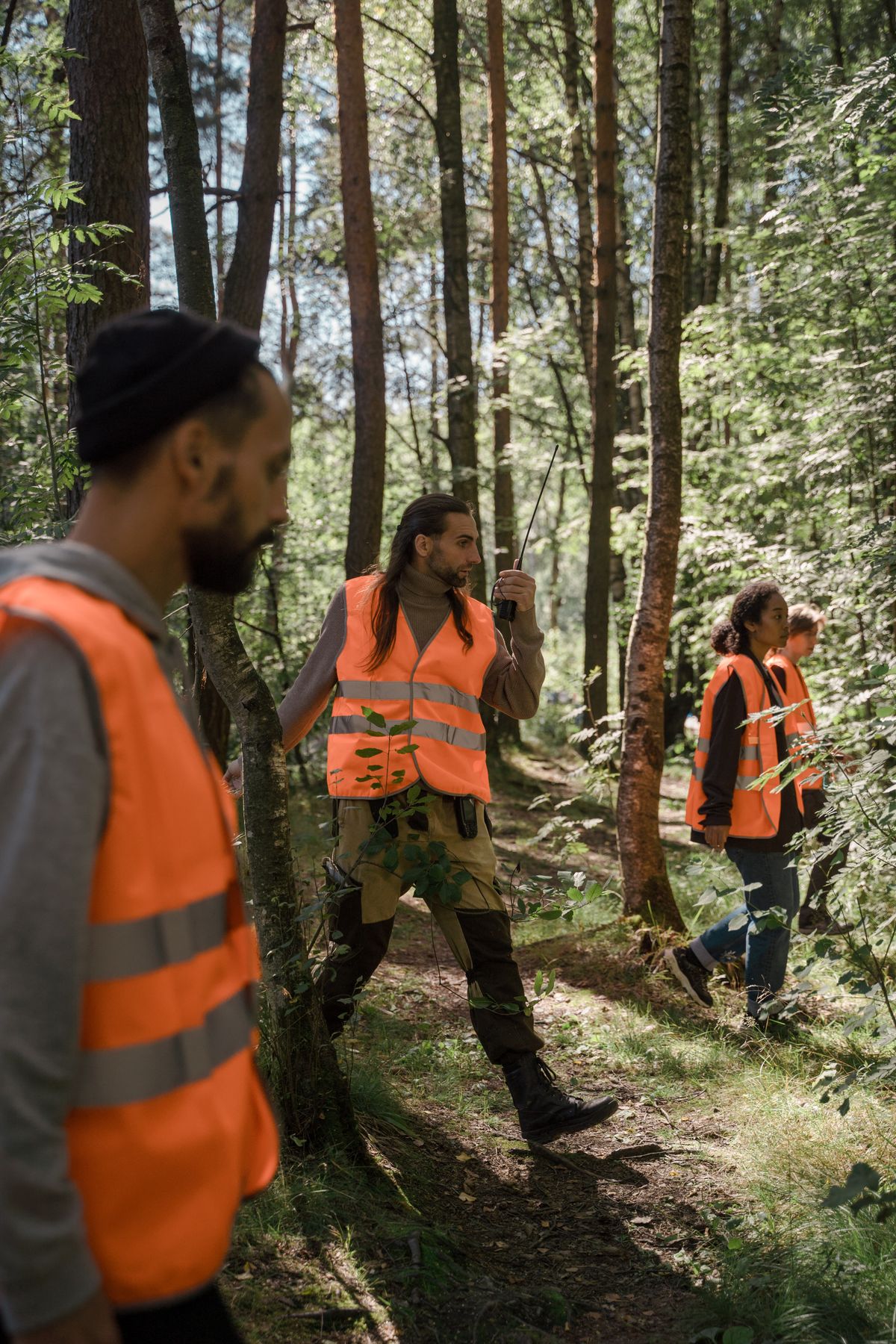 Volunteers in high-visibility vests walking a forest trail in an organized search line with radios