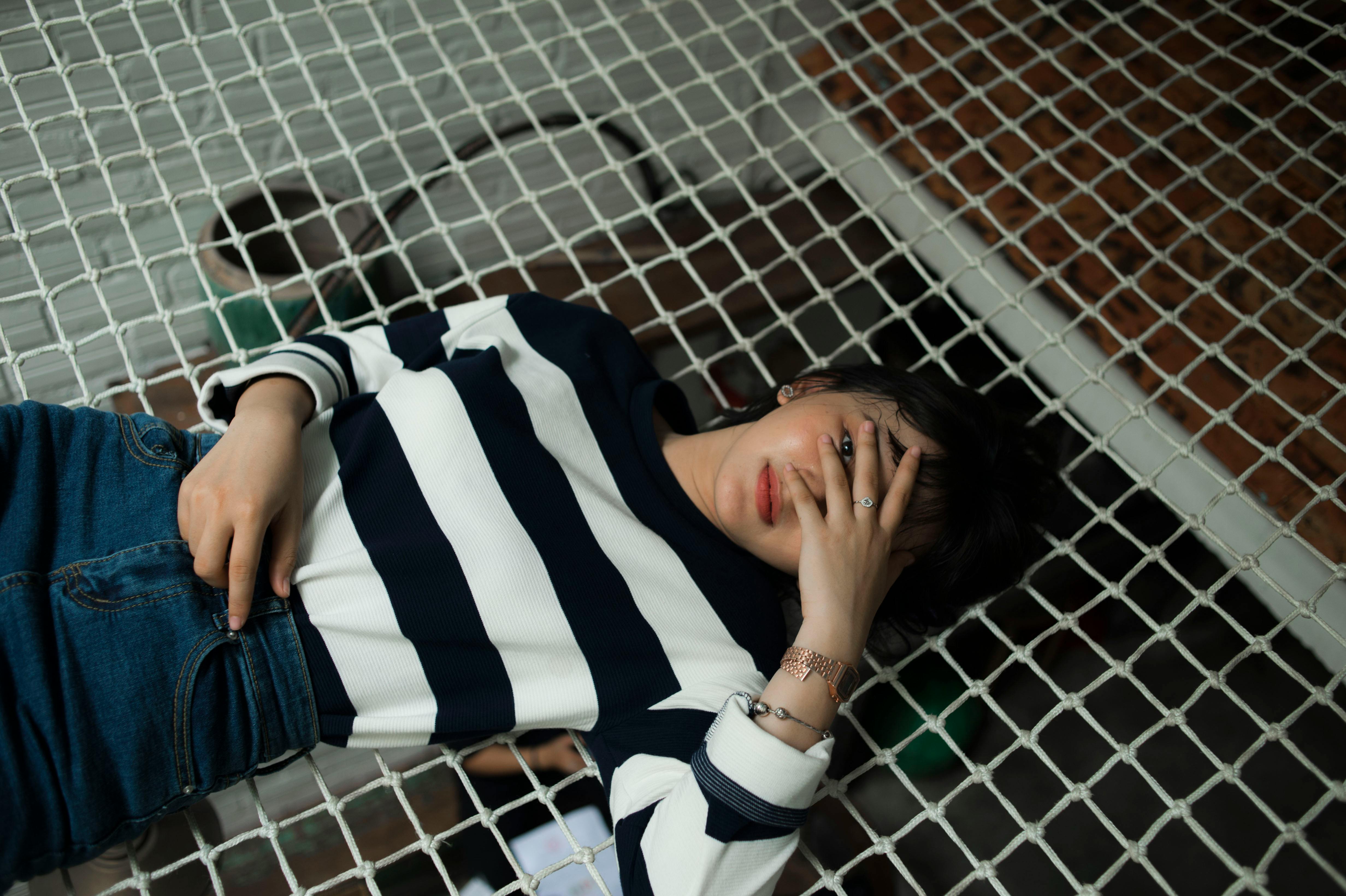 A young woman in striped top laying on a net indoors, exuding a relaxed vibe.