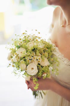 Bride in a white gown holding a delicate bouquet of white and yellow flowers at a wedding.