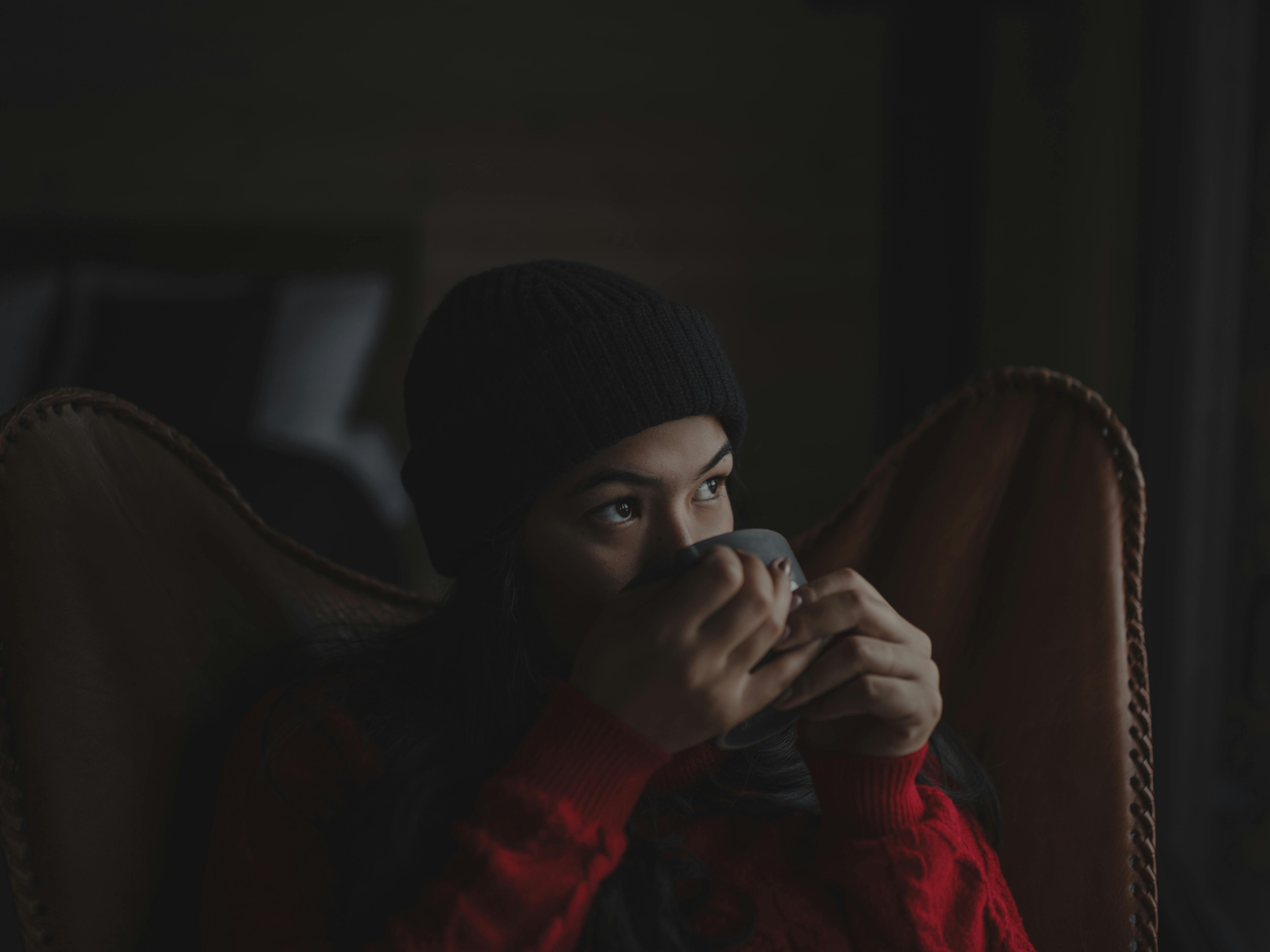 Woman in a winter sweater savoring a hot beverage indoors, creating a cozy atmosphere.