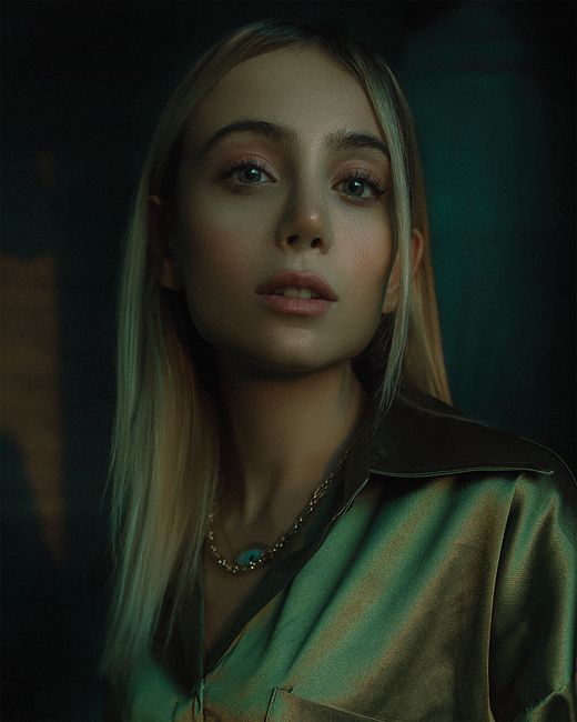 Striking portrait of a woman with blonde hair, stylish blouse, and necklace in soft lighting.