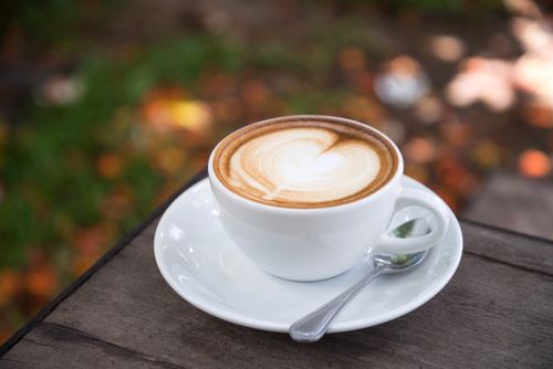 Free A beautifully crafted latte with heart art sits on a wooden table outdoors. Stock Photo