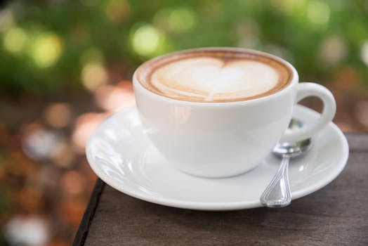 一杯精美的拉花拿铁放在户外，旁边有一把勺子，杯子是白色的