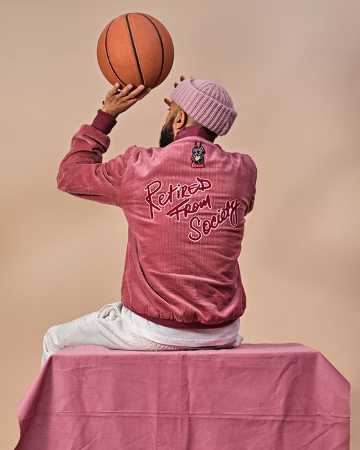 Bearded man in pink fashion with basketball, sitting in studio. Unique style and expression.