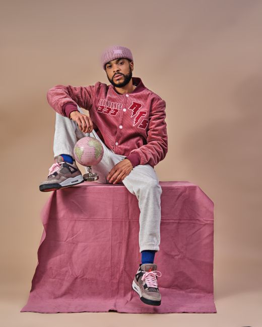 Stylish man in a textured studio setting wearing a pink jacket, holding a globe.
