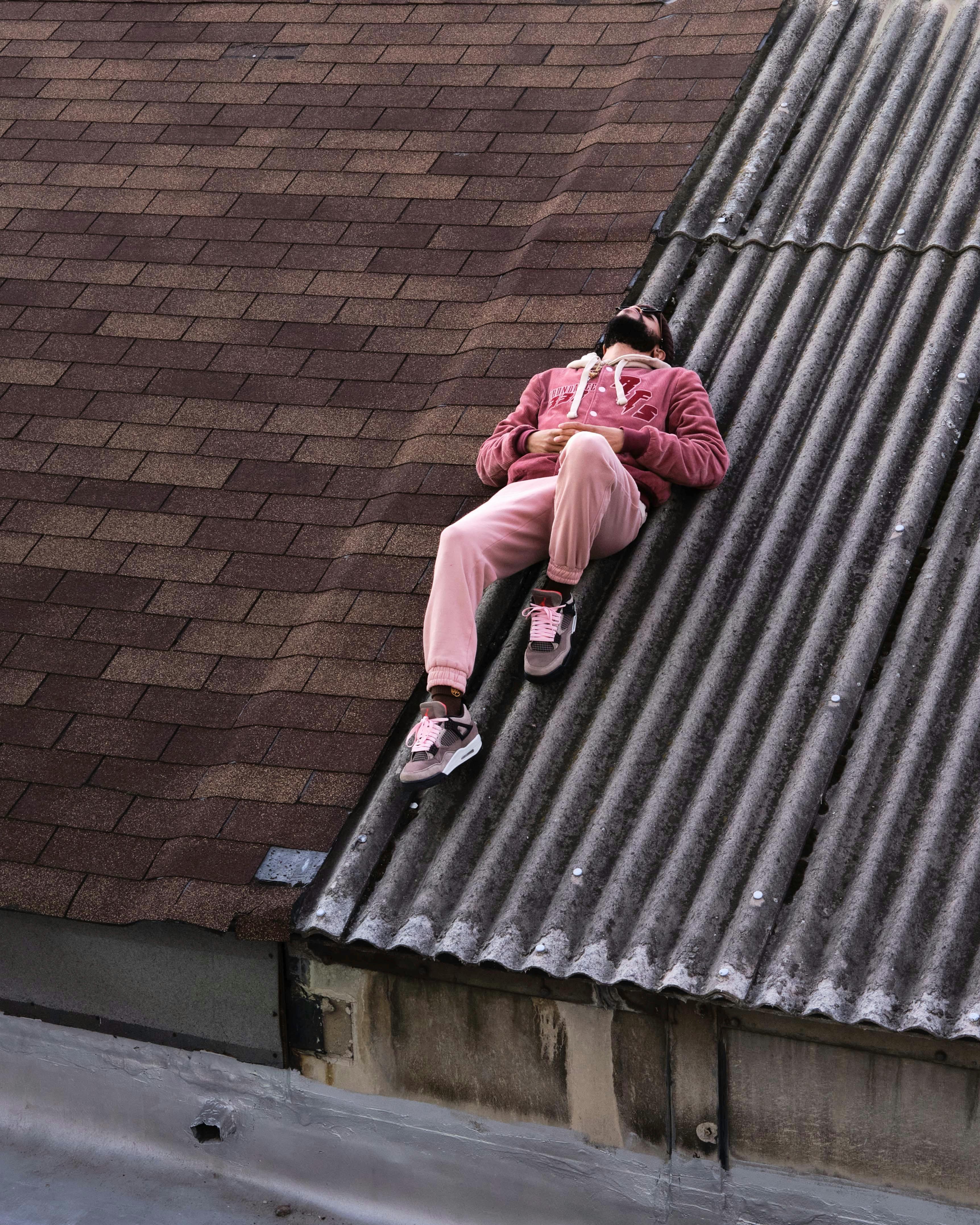 A man in pink attire lies relaxed on a corrugated rooftop, capturing urban leisure.