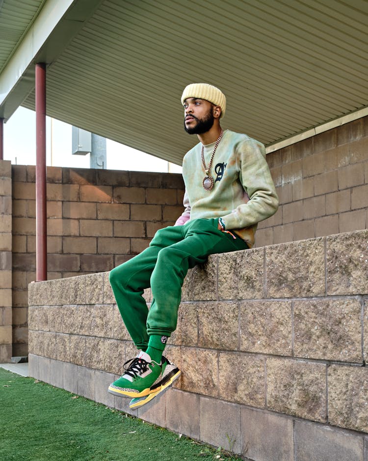 A Man In Green Joggers And Shoes Sitting On Concrete