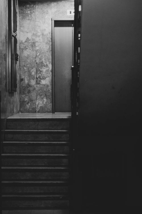 Free A black and white photograph of a dimly lit staircase leading to a closed door. Stock Photo