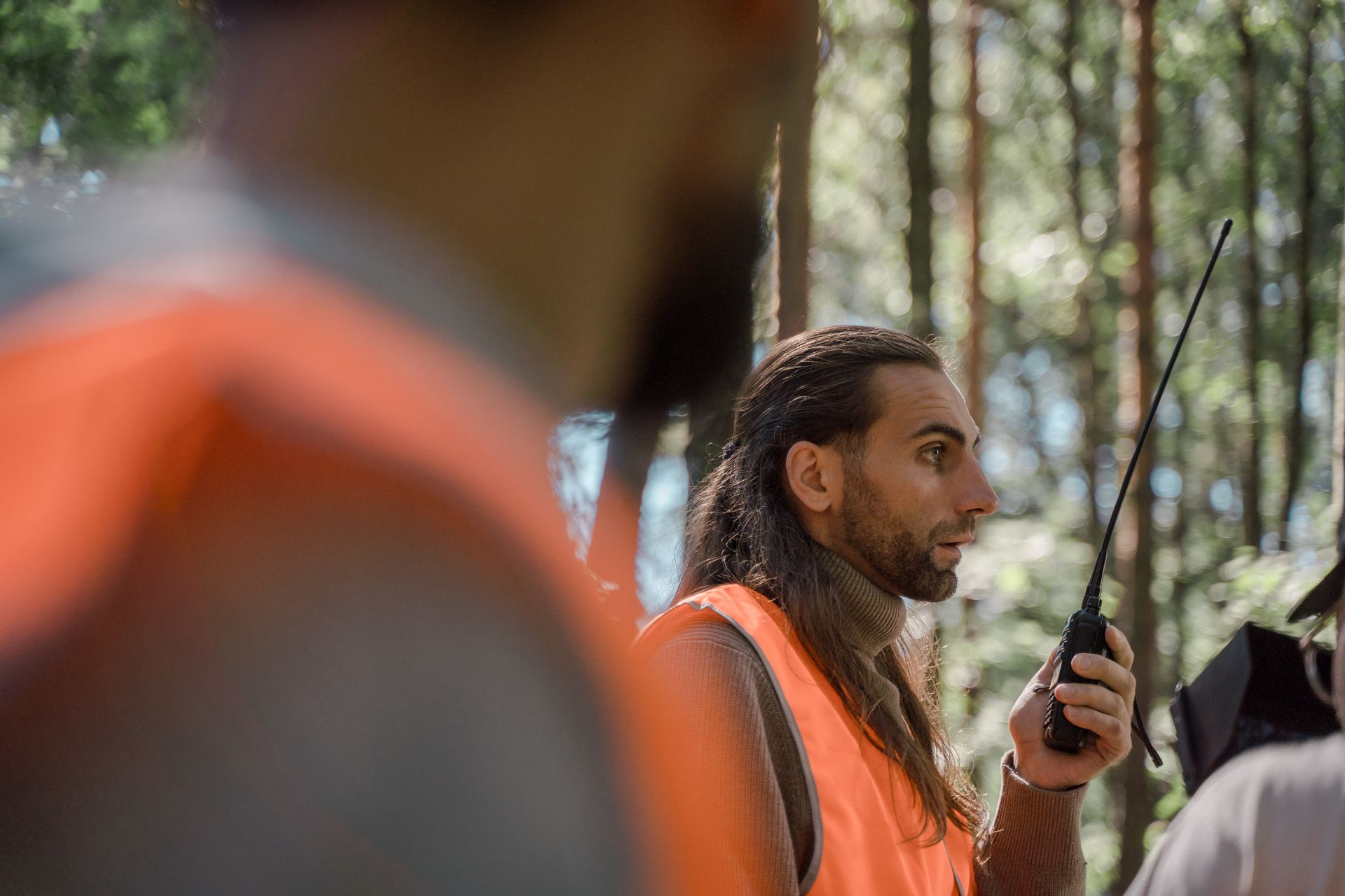 Men in high-visibility vests communicate using walkie-talkies in a forest setting.