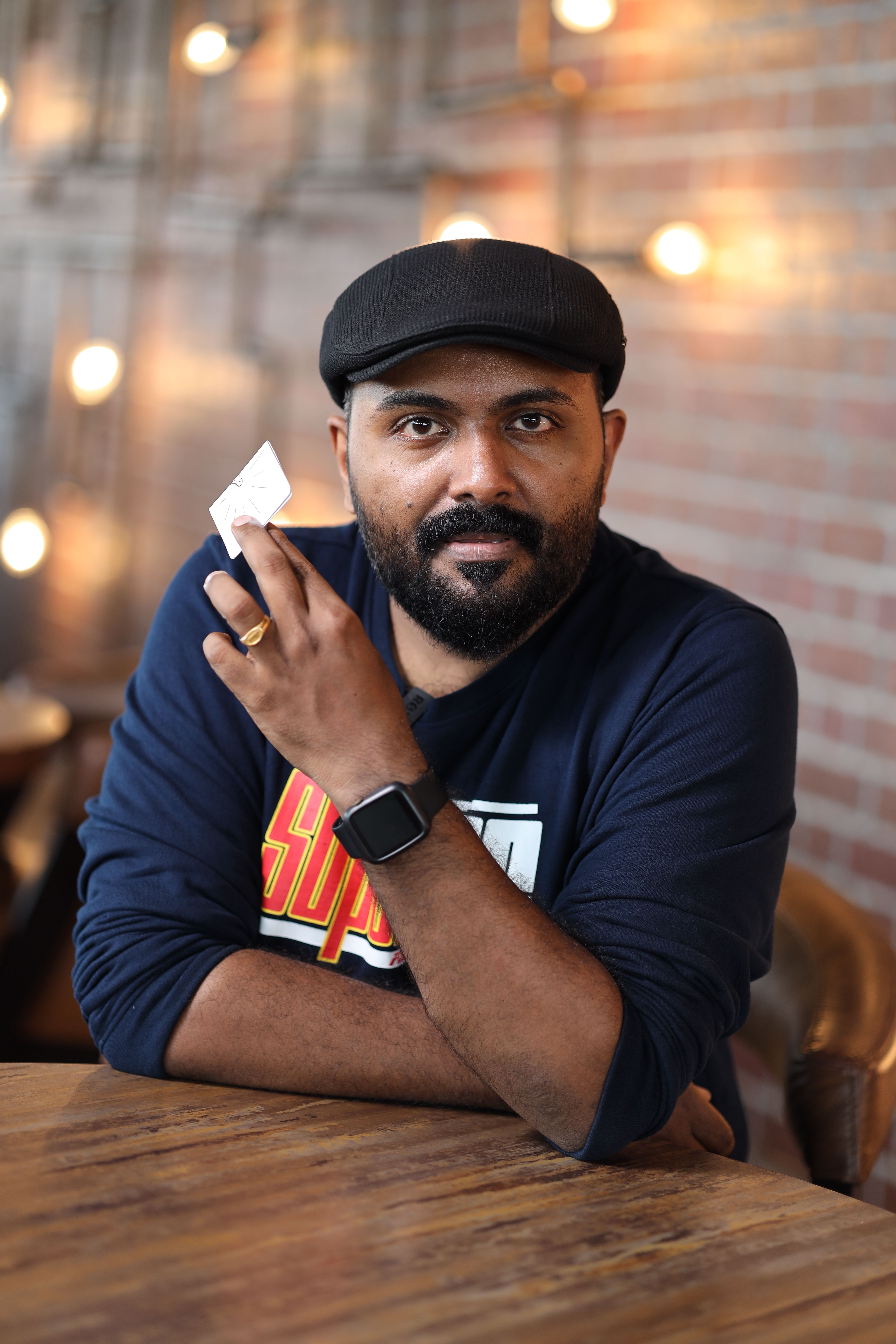 A casual portrait of a bearded man holding a note in a cozy café with warm lighting.