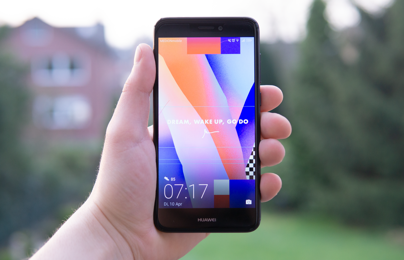 Hand holding a Huawei smartphone displaying a colorful screen outdoors in Germany.