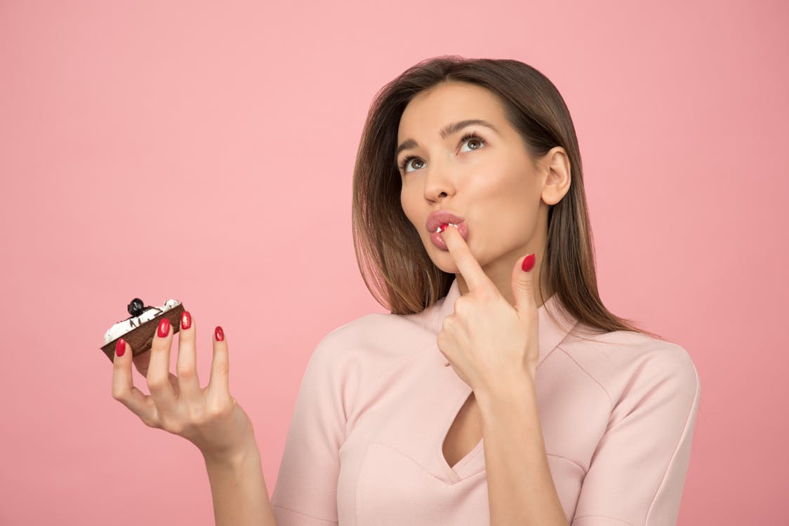 Vrouw Cupcake Eten Terwijl Staande In De Buurt Van Roze Achtergrond In Kamer
