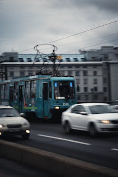 Blurry tram and cars in a bustling city street scene with overcast skies.