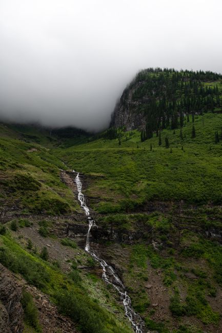 A serene mountain valley draped in mist with a tranquil waterfall cascading down lush greenery.