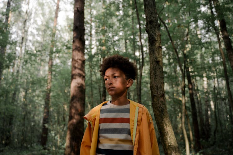 Sad Teenage Boy In Yellow Raincoat Standing In Forest