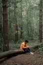 Sad Teenage Boy in Yellow Raincoat Sitting on Log in Forest