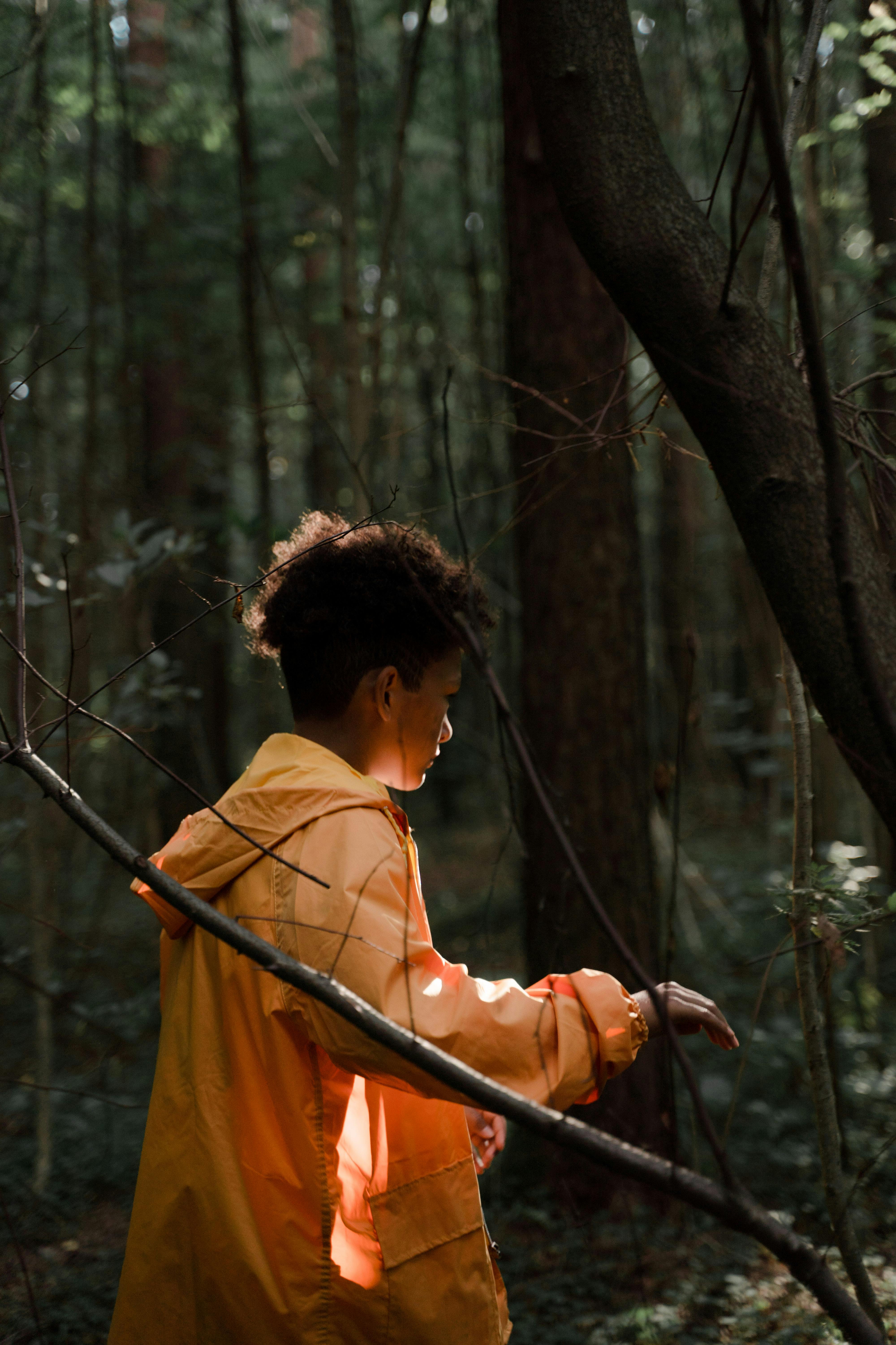 teenage boy in yellow raincoat walking in forest