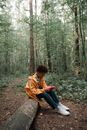 Sad Teenage Boy in Yellow Raincoat Sitting on Log in Forest