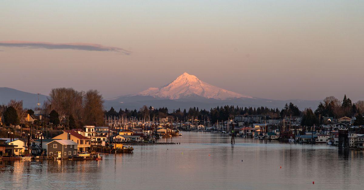A captivating view of Mount Hood at sunset with a serene marina and houses along the river in Oregon, USA.