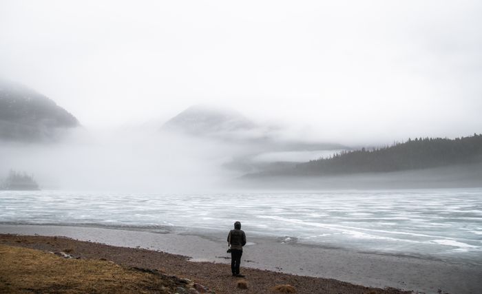 A solitary figure standing by a misty lake — reflection and quiet presence