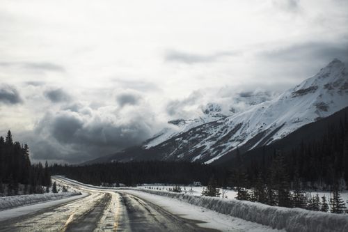 Free Snow-covered mountain road with dramatic clouds creates a moody alpine atmosphere. Stock Photo