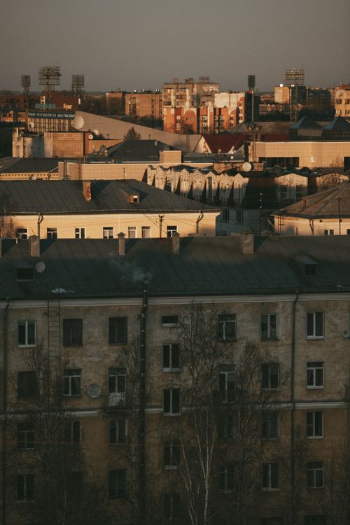 Free A cityscape featuring diverse rooftops and buildings lit by the warm glow of sunset. Stock Photo