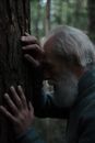 Profile of Senior Man with White Beard Leaning against Tree Trunk in Forest