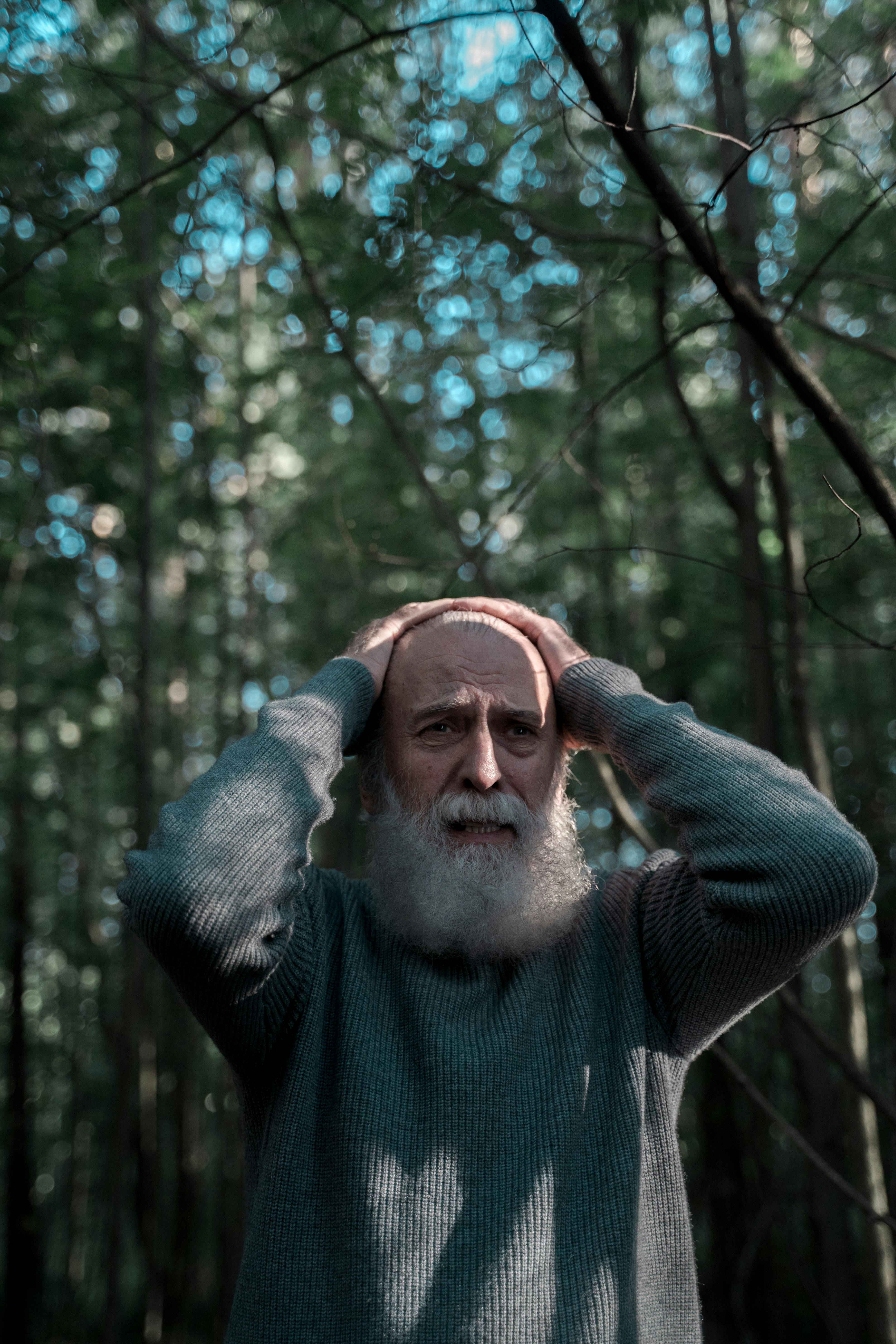 An elderly man looks concerned, standing in a sunlit forest.