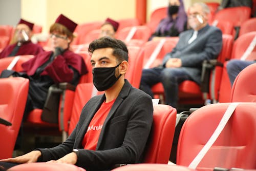 Man in Black Blazer Wearing Face Mask Sitting Inside Auditorium