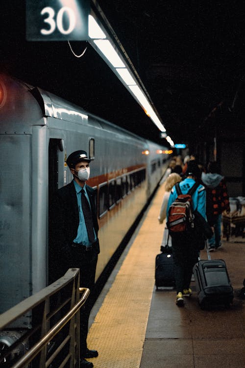 A Man in Black Jacket Wearing Face Mask Standing Beside Train