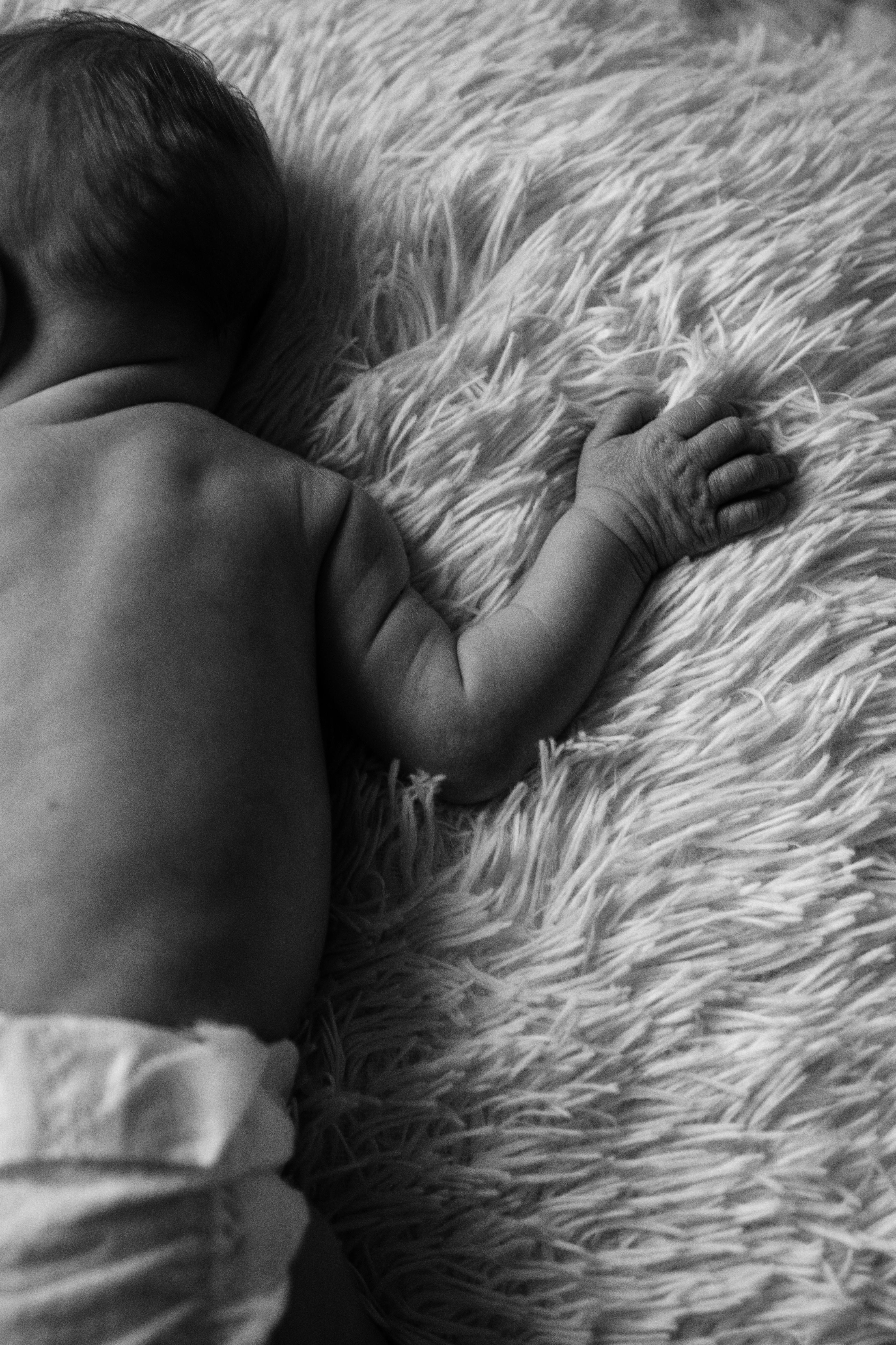 grayscale photo of a baby lying on furry carpet