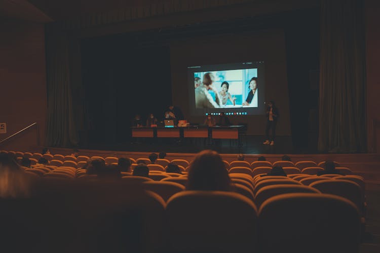 A Group Of People On Stage Showing A Video On Big Screen