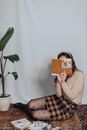 Woman with Face Obscured by Book Sitting on Carpet 