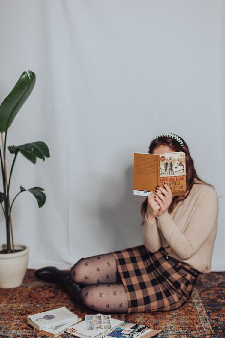 Woman With Face Obscured By Book Sitting On Carpet 