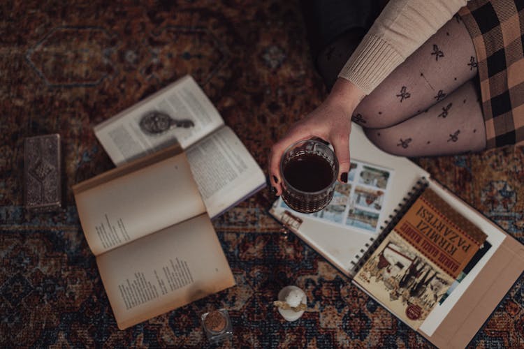 Woman Sitting On Carpet Surrounded By Books And Keepsakes Holding Glass