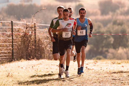 Group of four male athletes competing in an outdoor running race on a grass field.