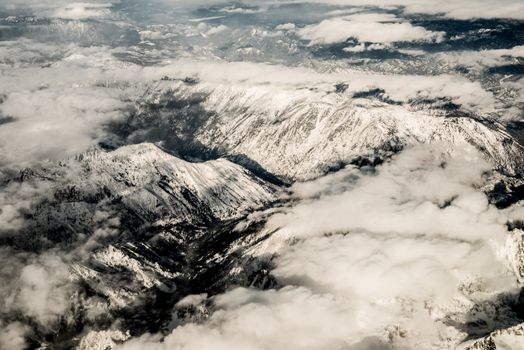A breathtaking aerial view of snow-covered mountains peeking through clouds, creating a serene winter landscape.