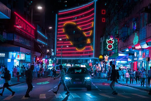 A bustling night street scene in Hong Kong with neon lights and pedestrians crossing.