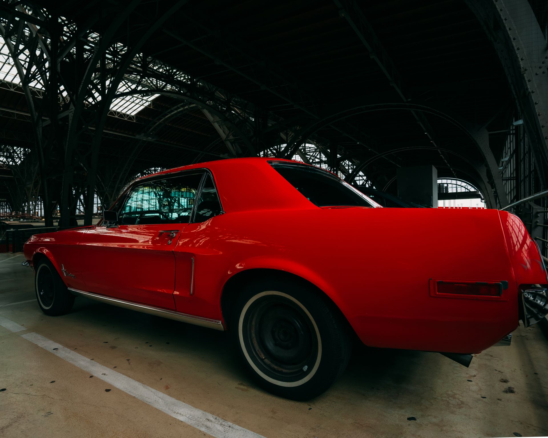 Classic red coupe parked in an industrial garage with steel beams overhead, highlighting vintage design.