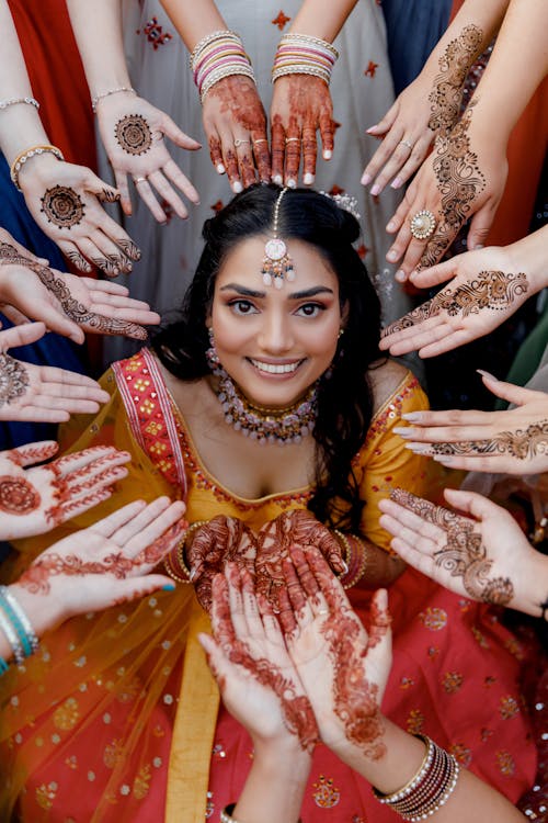 Hands Decorated in Henna Tattoos Forming Circle Around Smiling Woman Dressed in Traditional Indian Outfit