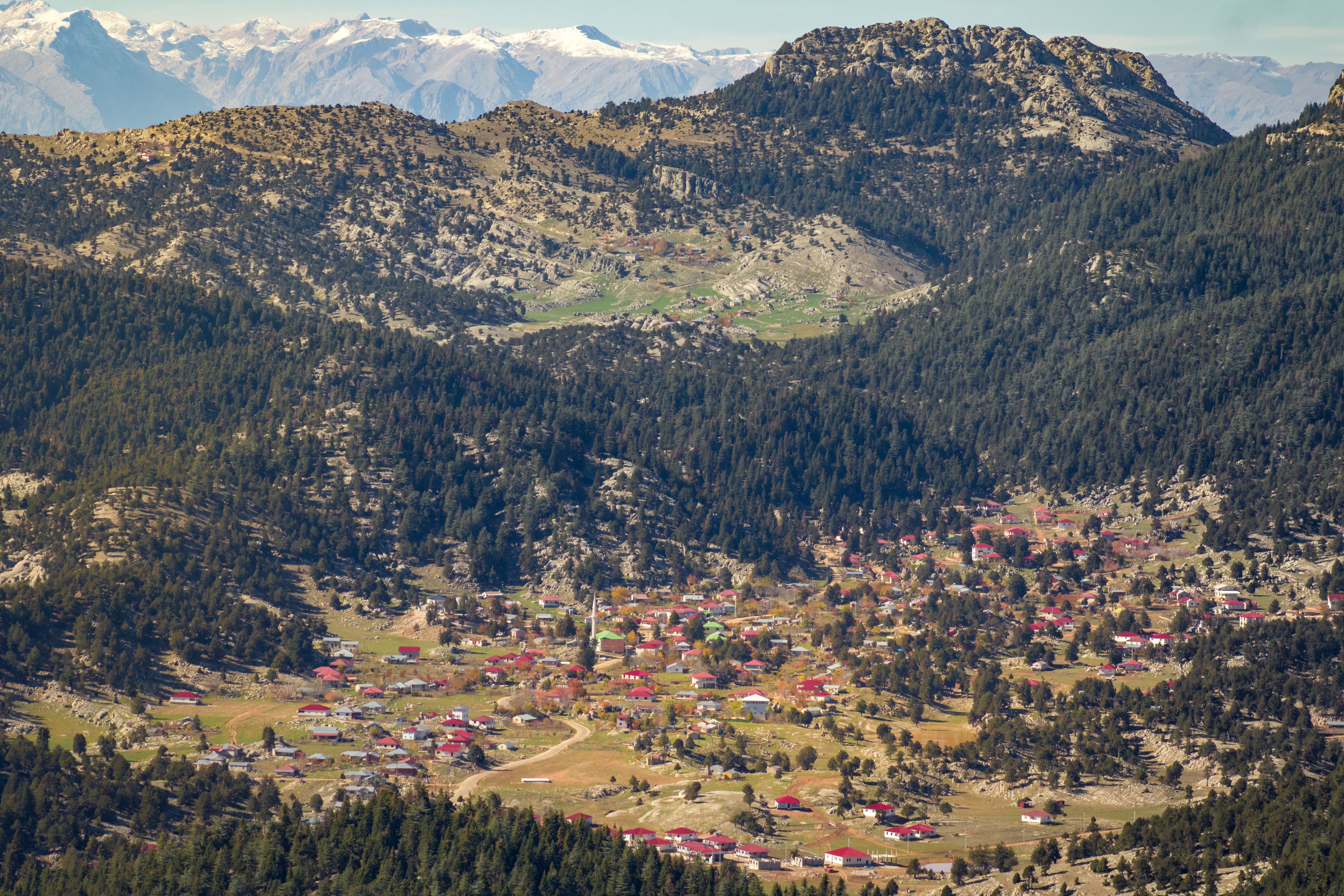 Breathtaking aerial shot of a rural village in Adana, Turkey, surrounded by mountains and lush greenery.